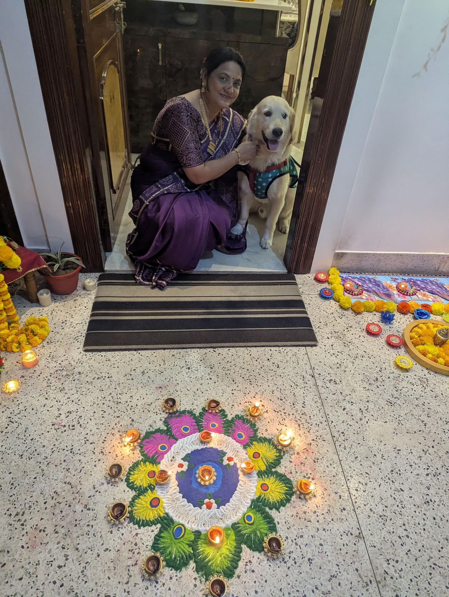 Maa kneeling beside Bruno at the Diwali doorway with rangoli.